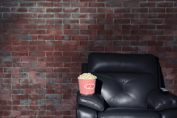 Cinema armchair with popcorn and remote control for home theatre on brick wall background. Watching movie