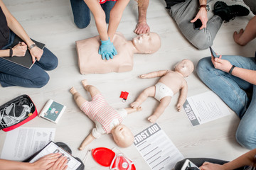 Group of people learning how to make first aid heart compressions with dummies during the training...