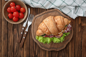 Wooden board with delicious croissant sandwich on table