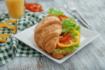 Plate with delicious croissant sandwich on wooden table