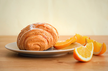 Plate with tasty croissant and orange slices on table