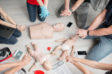 Group of people learning how to make first aid heart compressions with dummies during the training...