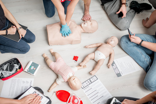 Group of people learning how to make first aid heart compressions with dummies during the training indoors