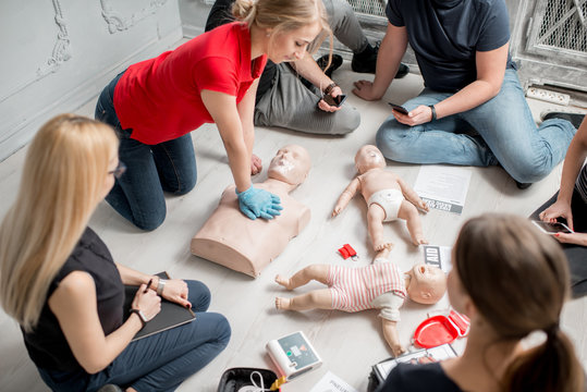 Young woman instructor showing how to make chest compressions with dummy during the first aid group training indoors