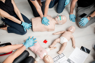 Group of people learning how to make first aid heart compressions with dummies during the training...