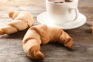 Tasty crescent rolls and cup of coffee on wooden background