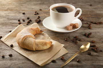 Tasty crescent roll and cup of coffee on wooden background