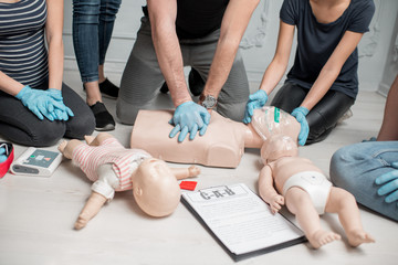 Group of people learning how to make first aid heart compressions with dummies during the training indoors. Close-up view on the hands and dummies