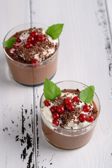 Chocolate mousse with currant and mint in a glasses on a whiite wooden background.