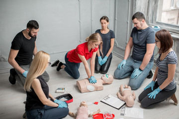 Group of people learning how to make first aid heart compressions with dummies during the training...