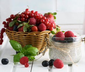 Healthy blended smoothie made from almond milk. Glass jar with chia pudding with fresh strawberries, raspberries and blueberries. Basket with berries. On a wooden light background.