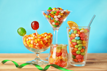 Glassware with different candies on table against color background