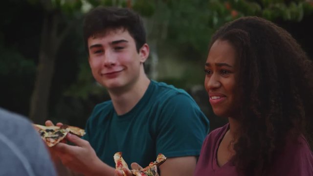 Teenage friends sit round a firepit eating take-away pizzas