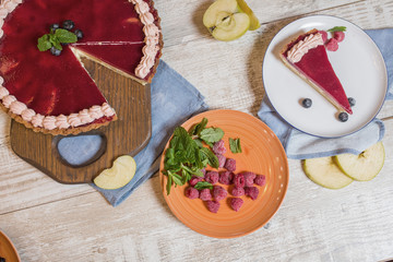 Cheesecake with jam on a wooden table, decorated with raspberries, slices of apples and mint