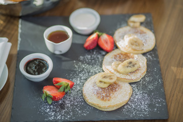 pancakes for breakfast with fresh strawberries and a banana sprinkled with powdered sugar, and three different sauces: jam, honey and condensed milk