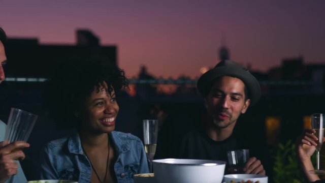 Friends sat round a table on a rooftop talking at dusk