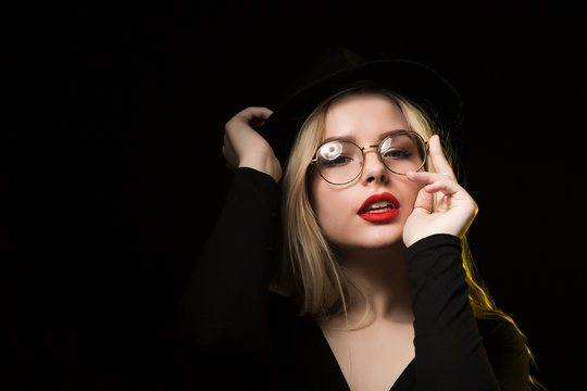 Fabulous young woman wearing black blouse, hat and glasses, posing in the shadow