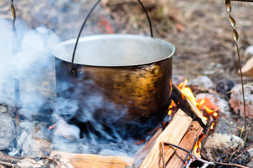Iron pot with food on a burning fire. Food in a metal cauldron is cooked on fire. Cooking food in...