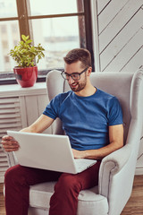 A happy young student sits on a chair and using a laptop.