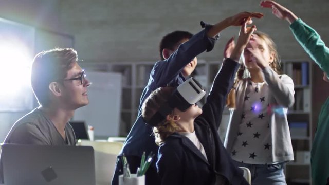 Group of four primary school children, one of them wearing VR glasses, having fun with virtual reality with their teacher at school - Powered by Adobe