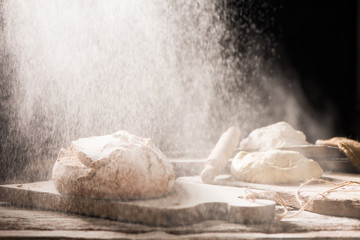 Freshly baked bread on wooden table on dark background with flour on the air