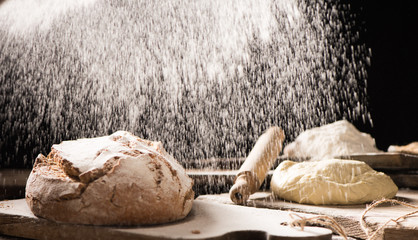 Freshly baked bread on wooden table on dark background with flour on the air
