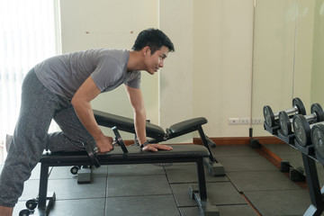 Handsome man playing with dumbbell in gym. Bodybuilder man doing heavy weight exercise with dumbbell in fitness club.
