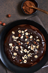 Chocolate cake with hot chocolate sauce and fried hazelnuts on a dark, concrete background.
