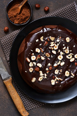 Chocolate cake with hot chocolate sauce and fried hazelnuts on a dark, concrete background.
