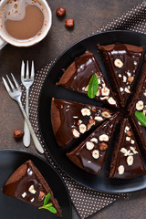 Chocolate cake with hot chocolate sauce and fried hazelnuts on a dark, concrete background.