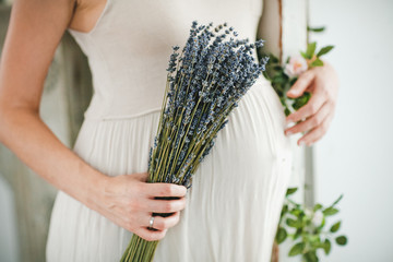 Pregnant woman with bouquet of lavender flowers holds hands on belly outdoors. Pregnancy,...