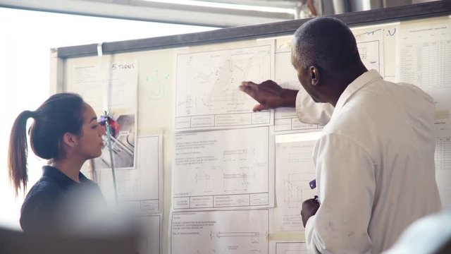 Tutor Discussing Technical Drawings With Apprentice Engineer 