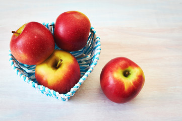Red apples in a basket on a white wooden background