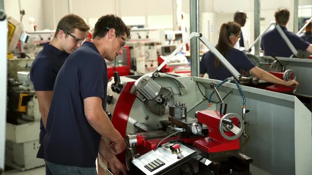 Apprentice Engineers Using Machinery In Manufacturing Plant