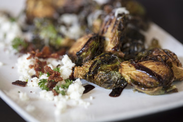 An appetizer plate of roasted Brussels Sprouts garnished with Feta cheese and bacon, with a drizzle of Balsamic Glaze