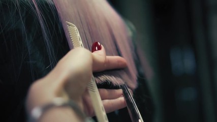 Hairdresser softly cuts female's long pink hair with professional scissors in hair salon. Colseup, slow mo