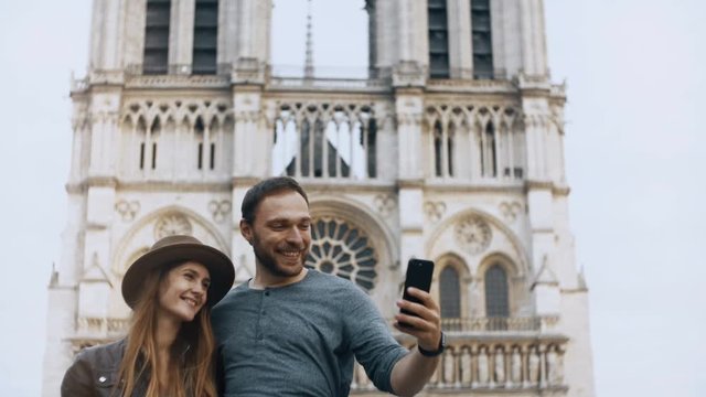 Young happy couple taking selfie photos on smartphone near the Notre Dame in Paris, France, enjoying the beautiful view.