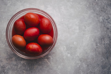 Set of six colored red inside a glass bowl for Easter holidays, coloring with red tint eggs over a gray concrete background