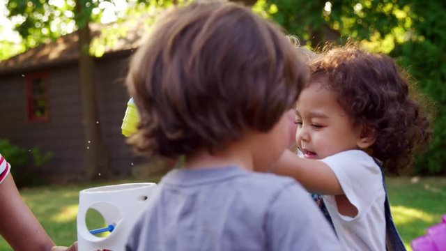 Mother And Young Children Playing With Water Table In Garden