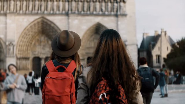 Two happy female walking with red backpacks near the Notre Dame, famous cathedral or church in Paris, France.
