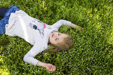 Happy little girl dreams on a green flowering  lawn