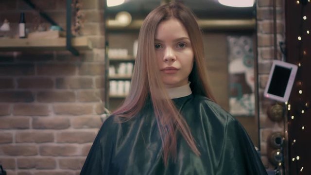 Beautiful woman turns around on chair in hair salon, swings her long pink and red hair and sends a blow kiss to the camera. Slow mo