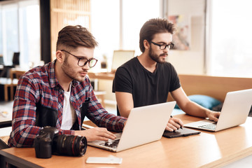 Fototapeta na wymiar Two freelancer men working at different laptops at desk.