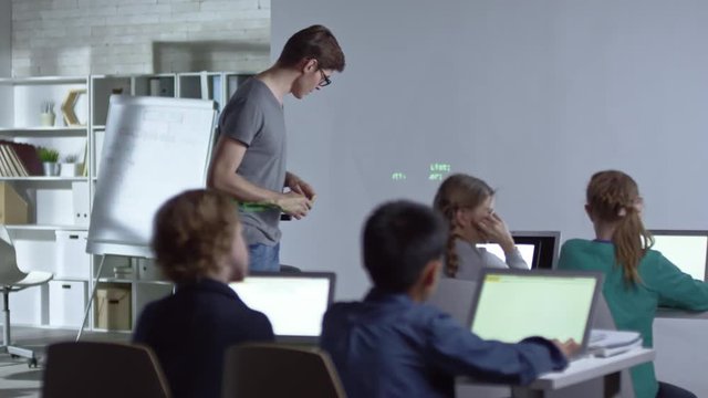 Four children of primary school age sitting in computer coding class, listening to their teacher and answering his questions