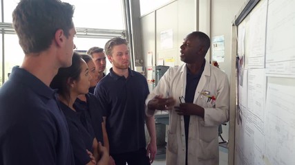 Tutor Discussing Technical Drawings With Apprentice Engineers 