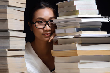 Girl in white shirt reading many textbooks on table with many high stacking