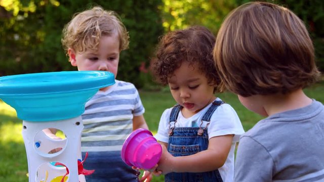 Group Of Young Children Playing With Water Table In Garden
