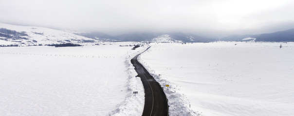 Fototapeta na wymiar Long road stretches through the snowy landscape, aerial view