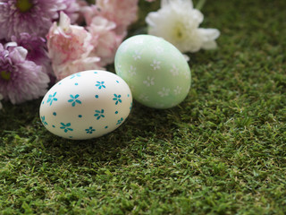 Cute hand painting Easter eggs with white color and blue flower pattern and green color and white flower pattern on egg shells, with pink and purple color flower background, on green grass