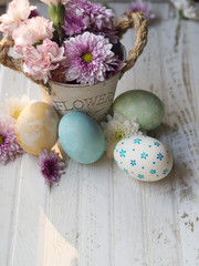 Obraz na płótnie Canvas Vertical copy space and background of yellow, blue and green painted Easter eggs with beautiful vintage Spring flowers pot on vintage white wooden table background, top view